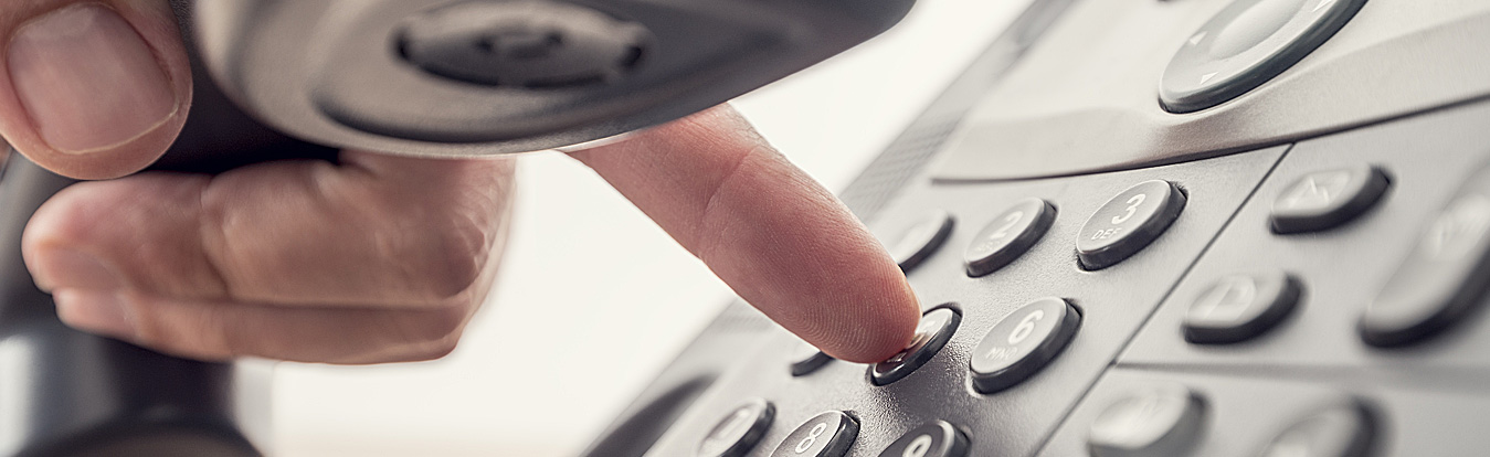 Photo of a person's hand holding a phone and dialing a phone number.