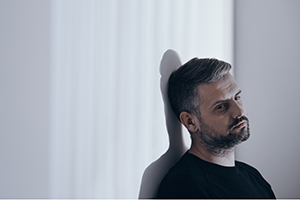 A somber man leaning against a wall.